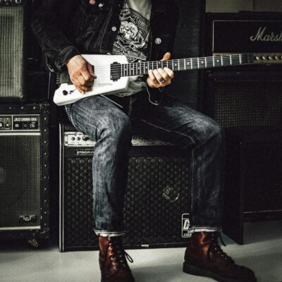 Man Sitting on Guitar Amplifier Playing Electric Guitar